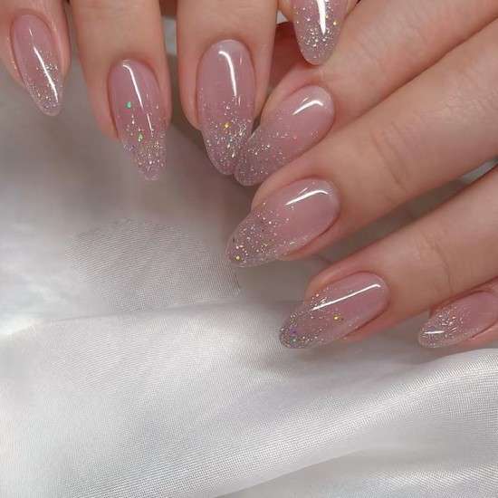Unhas transparentes com glitter.