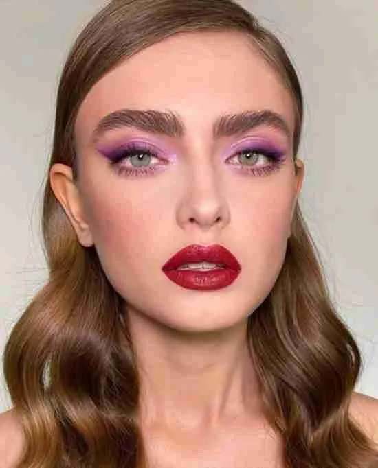 Maquiagem com sombra roxa e batom vermelho.